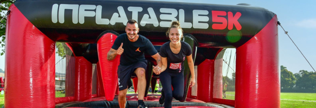 Man and women holding hands and smiling whilst running through an inflatable course.